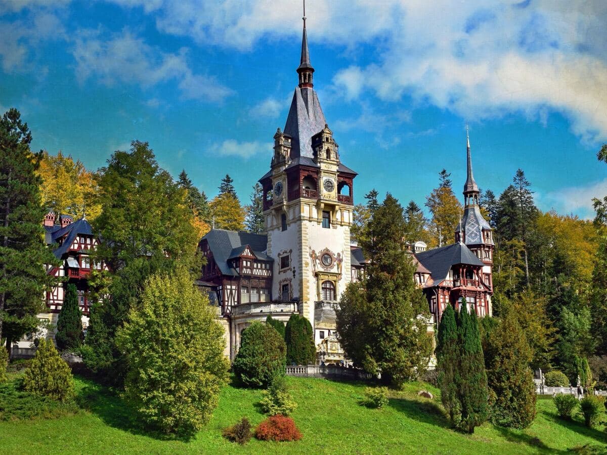 Castelul Peleș din Sinaia, văzut de pe pajiștea de dedesubt, între copacii de toamnă